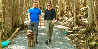 Two people walking dog on gravel trail.