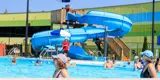 People in swimming pool and kids using spiral slide.